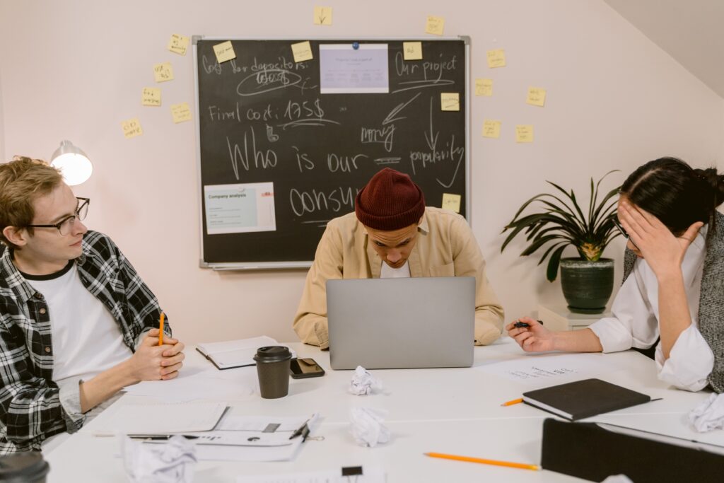Three colleagues engage in focused discussion with laptops and notes in a modern office setting.